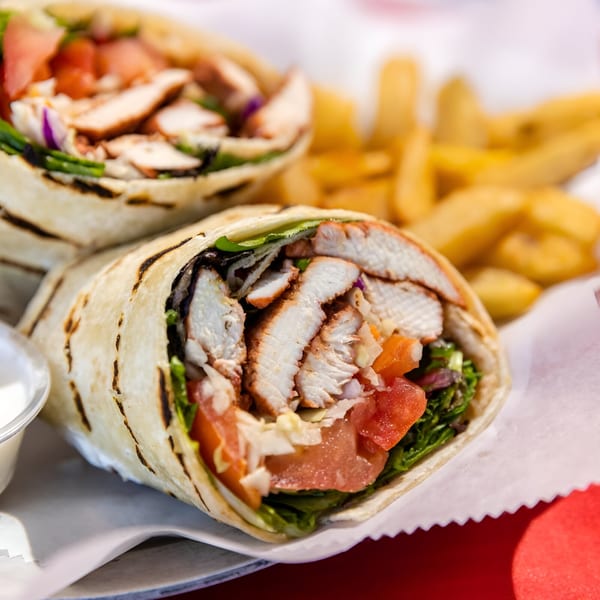 Two grilled chicken wraps with lettuce, tomato, and onion, served with fries and dipping sauce.