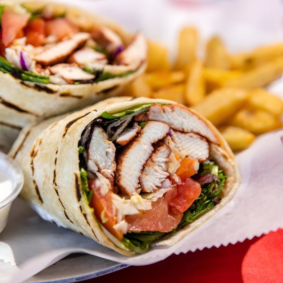Two grilled chicken wraps with lettuce, tomato, and onion, served with fries and dipping sauce.