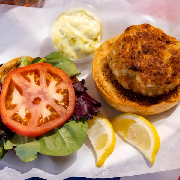 Go Fish! crab cake sandwich with lettuce, tomato, lemon wedges, and tartar sauce.