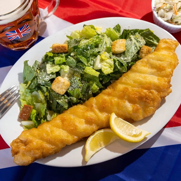 Golden-brown fried fish with lemon wedges and a Caesar salad on a white plate.