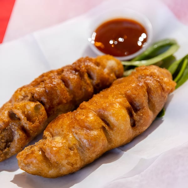 Two golden-brown battered fish pieces, with a side of dipping sauce and green garnish.