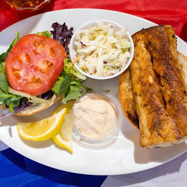 Go Fish! fish sandwich with tomato, lettuce, coleslaw, tartar sauce, and lemon wedges.